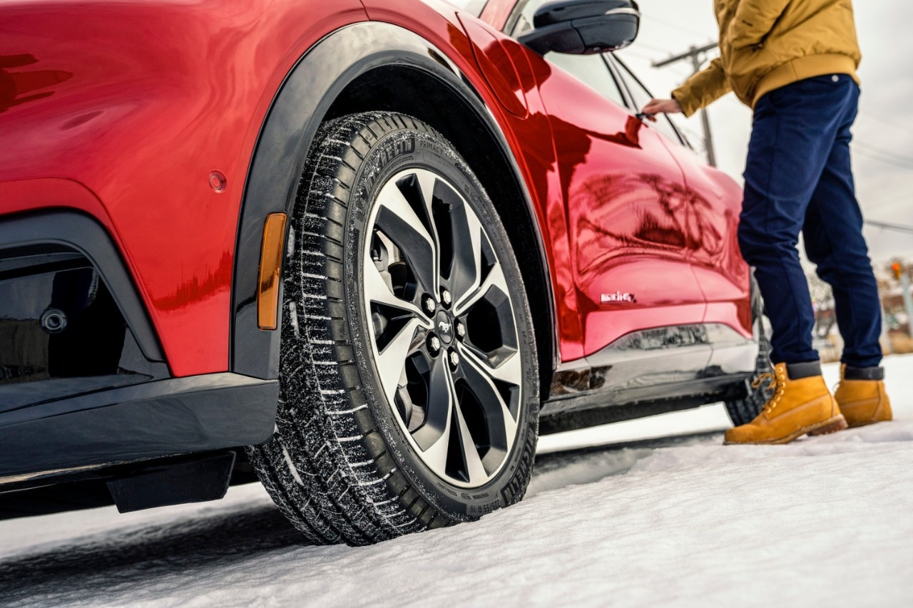 Official Ford winter photo showing a red Mustang Mach-E wheel on snow and a person reaching for the door handle