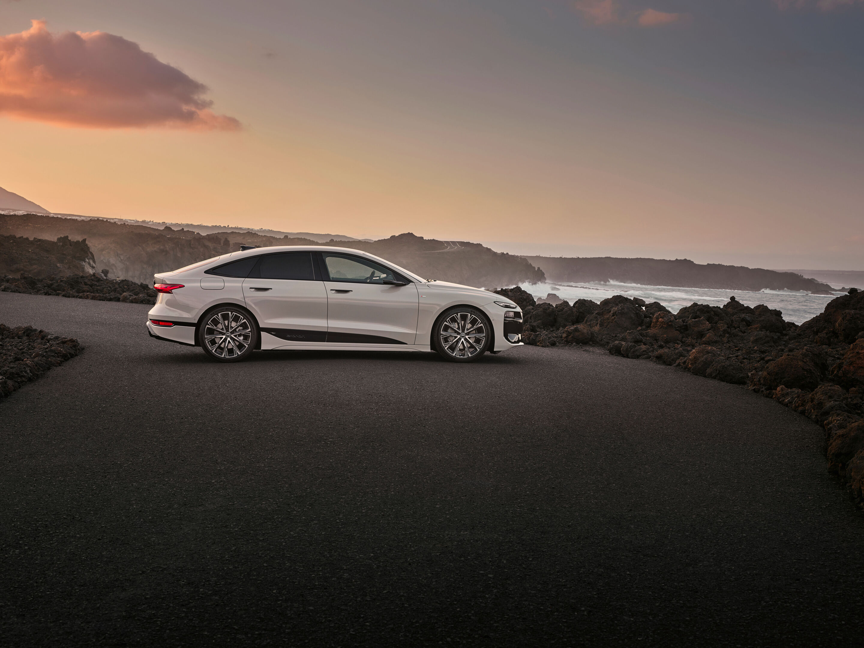 Audi A6 Sportback e-tron official side-profile image on a coastal road at sunset