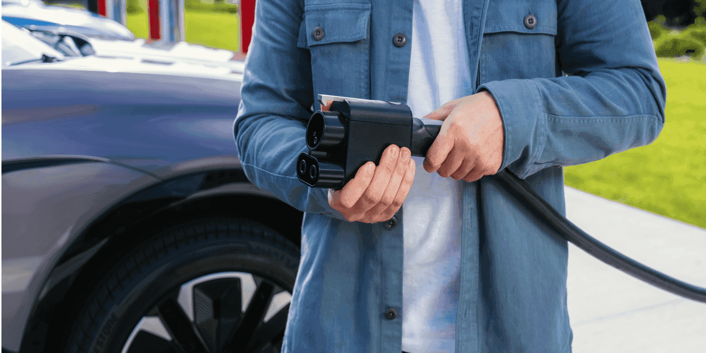 Driver holding an EV charging connector near an electric vehicle