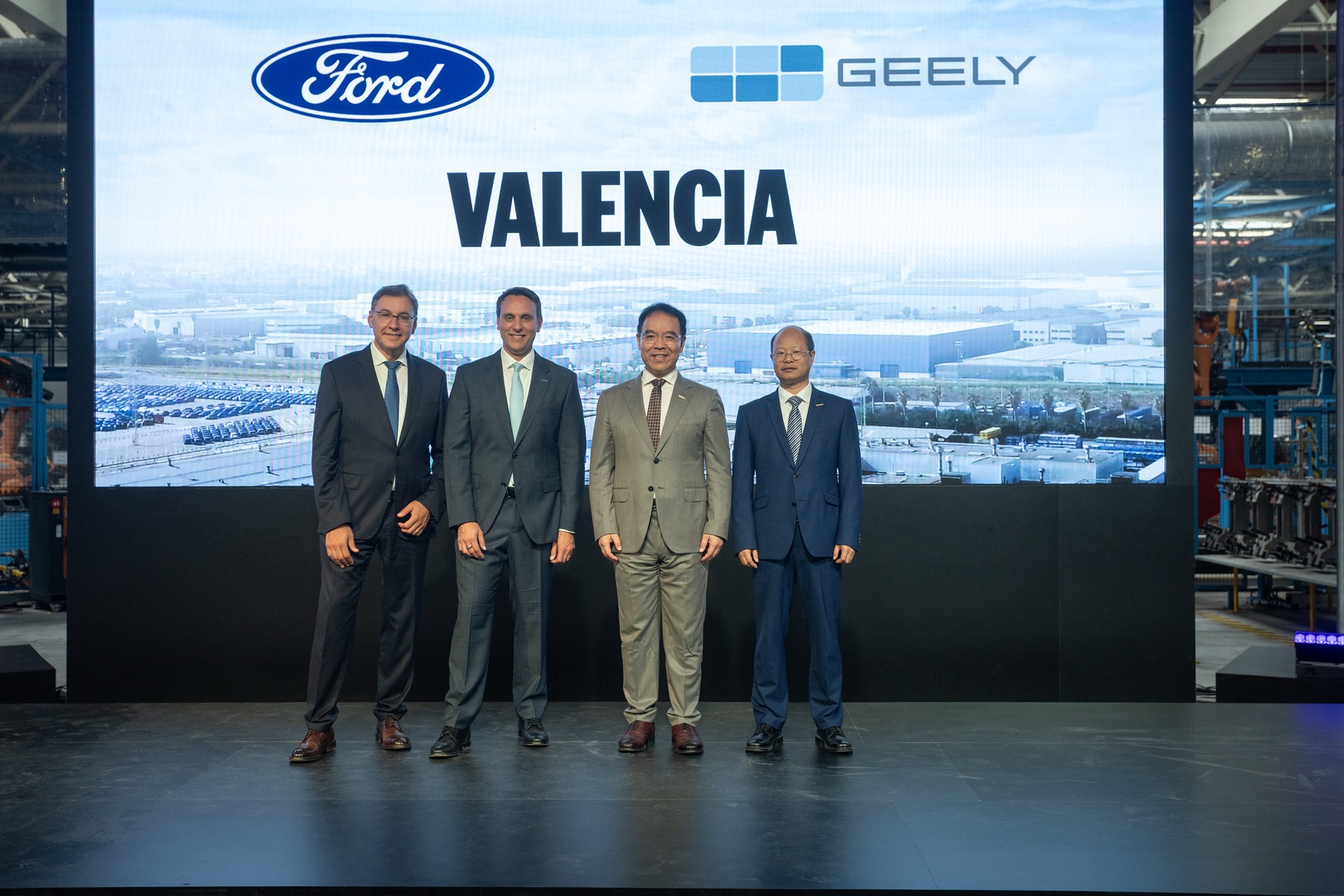 Ford and Geely executives at the Valencia factory with both companies' logos behind them