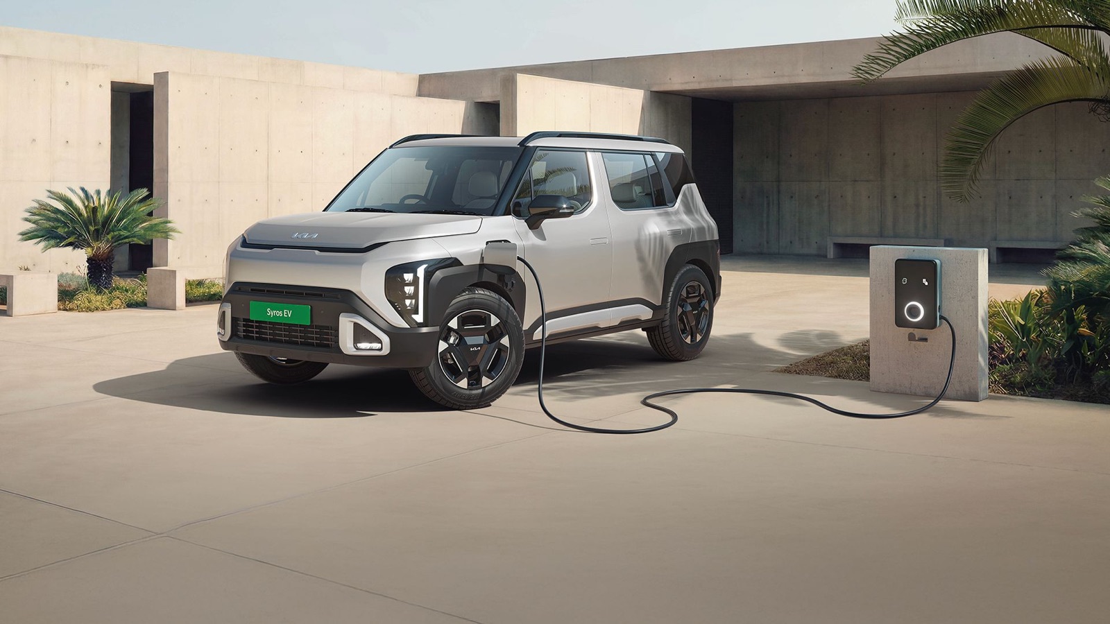 Official Kia image of a silver Syros EV plugged into a home charging station